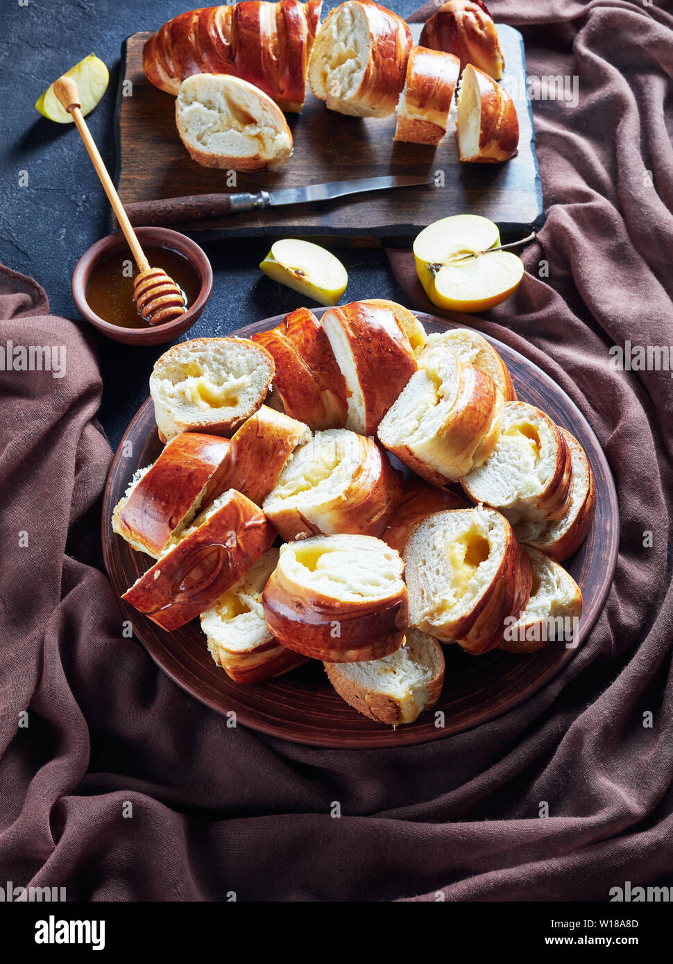 Les brioches avec remplissage confiture de pommes sur une plaque de faïence sur une table de cuisine en bois rustique avec tissu marron et le miel dans un bol, vue verticale d'un Banque D'Images