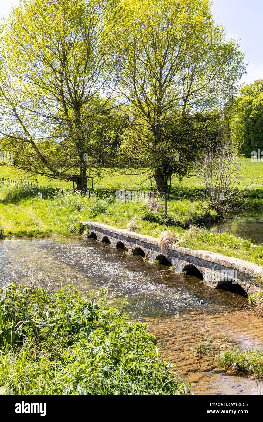 Un vieux pont de pierre à travers le ruisseau de Sherborne près du village de Cotswold, Sherborne Gloucestershire UK Banque D'Images