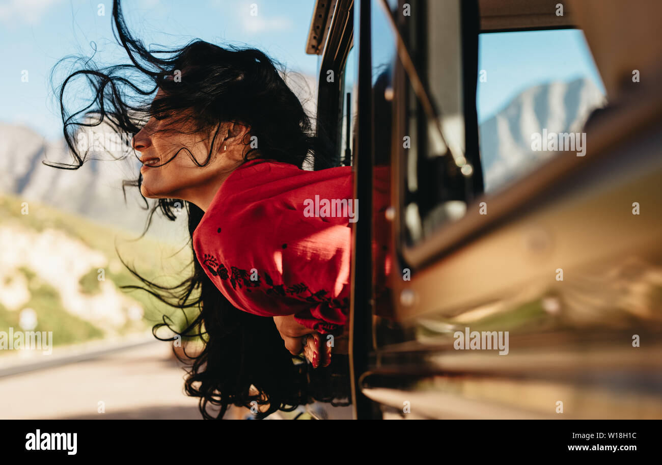 Belle femme assise sur sa voiture avec son visage par la fenêtre avec ses cheveux volant dans l'air. Femme profitant de la voiture d'un voyage en voiture. Banque D'Images