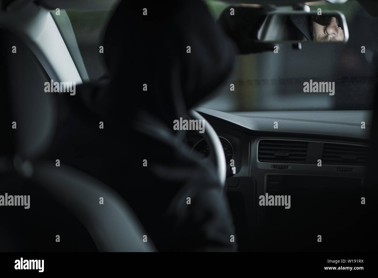 Grand Theft Auto Concept Photo with Caucasian voleur dans la trentaine déjà à l'intérieur de voiture volée en tenant regarder dans un miroir en arrière. Thème de l'automobile. Banque D'Images