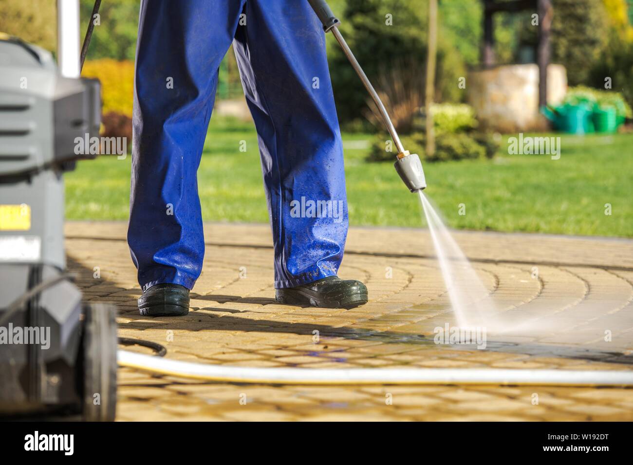 Travailleur et la rondelle de pression. Des hommes en manteau de pluie brique Nettoyage des chemins en utilisant le pulvérisateur d'eau puissant. Banque D'Images