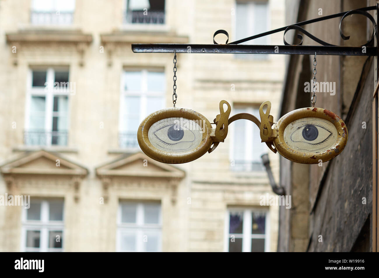 Paire de lunettes cerclées d'or, les yeux bleus - creative design enseigne suspendue au-dessus d'un magasin opticiens dans une rue de Bordeaux Banque D'Images