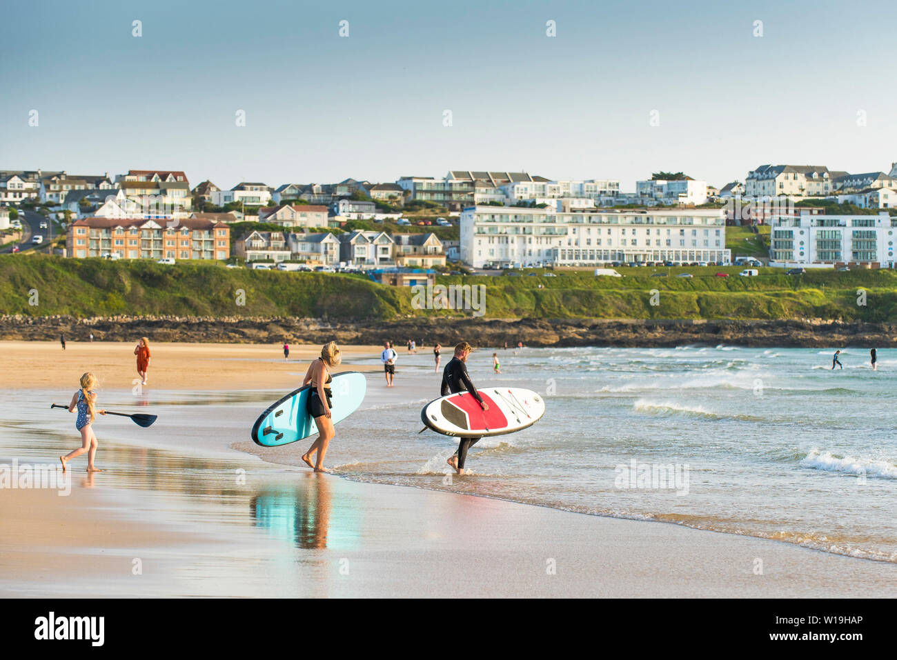 Les vacanciers transportant paddle boards dans la mer à la plage de Fistral à Newquay en Cornouailles. Banque D'Images