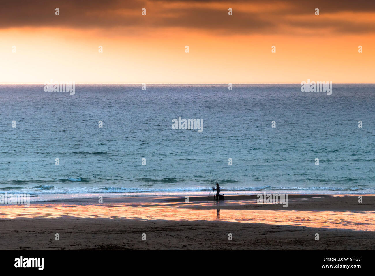 Un pêcheur solitaire la pêche à pied lors d'un coucher de soleil intense dans Fistral Newquay en Cornouailles. Banque D'Images