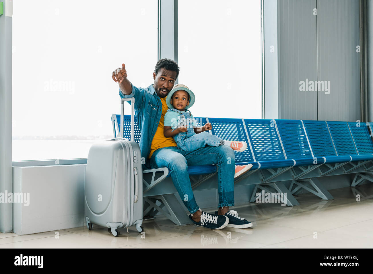 African American father sitting avec fils en aéroport et pointage du doigt Banque D'Images