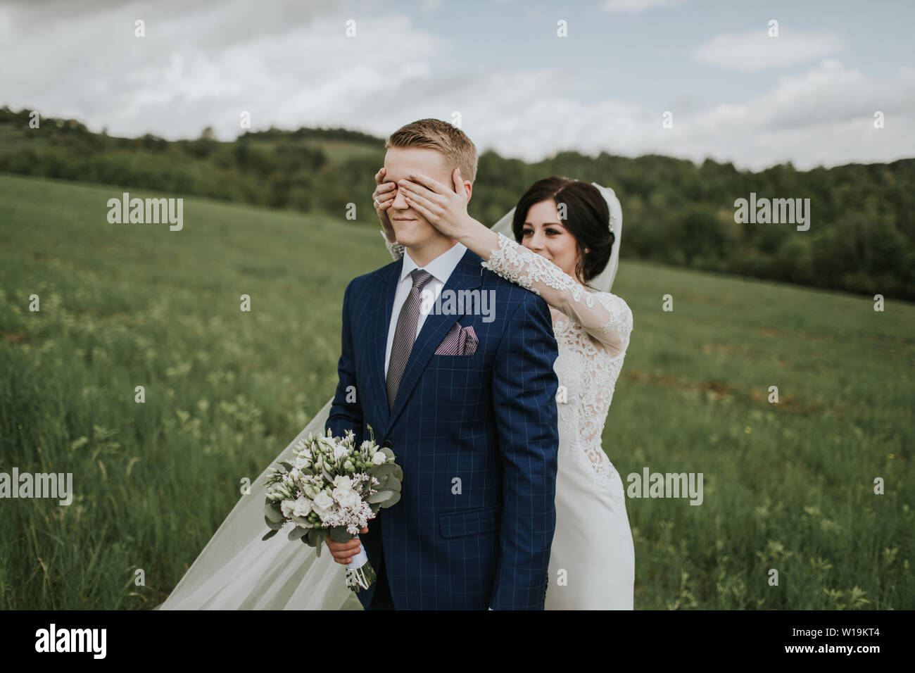 Les yeux du marié mariée couvrant. Cheerful groom standing on meadow et bride couvrant ses yeux de derrière. Banque D'Images