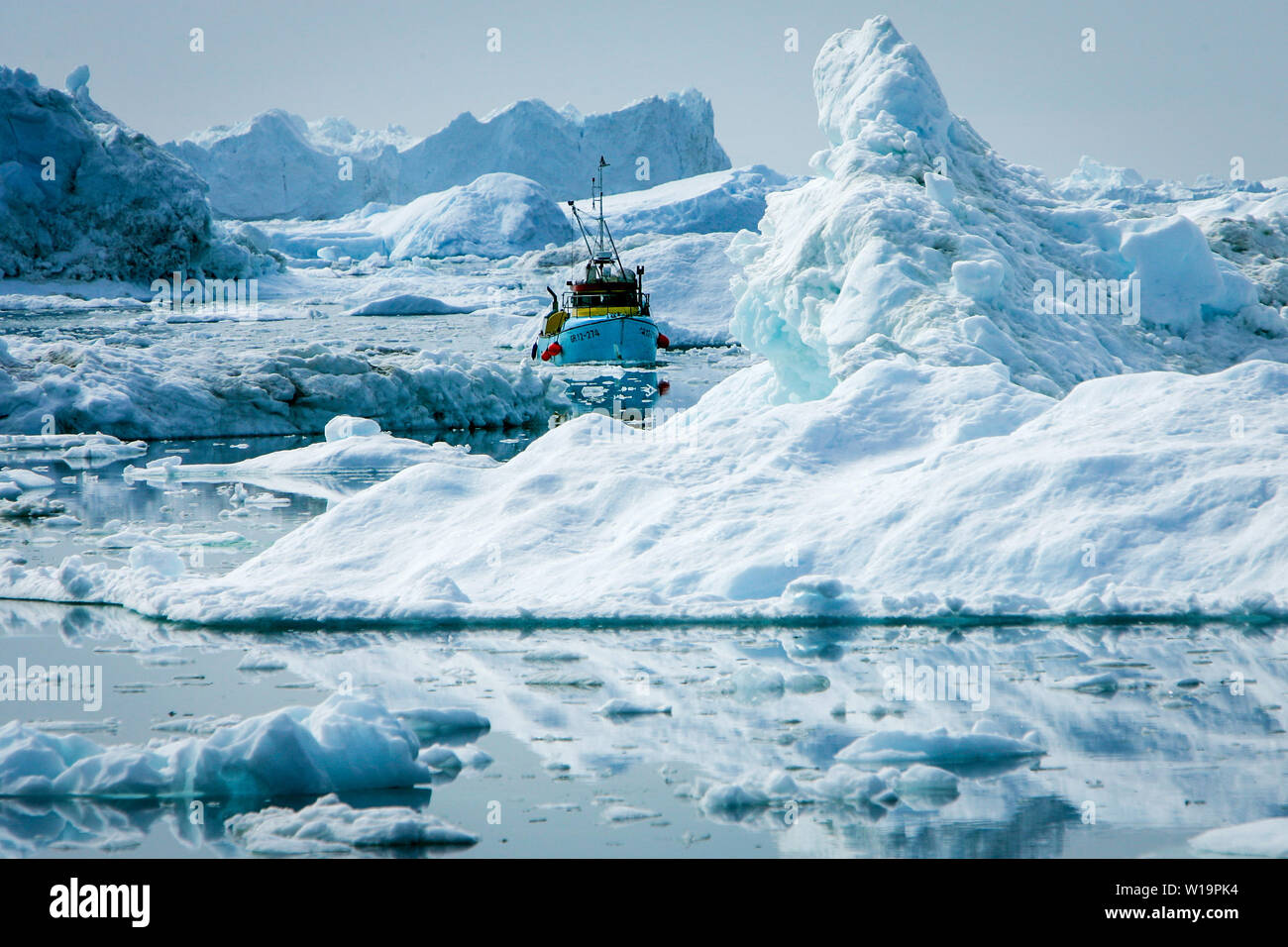 Les glaciers du Groenland sont en train de fondre. Bateau de pêche de manœuvres en zig zag entre les icebergs du glacier Sermeq Kujalleq, alias le glacier d'Ilulissat. Banque D'Images