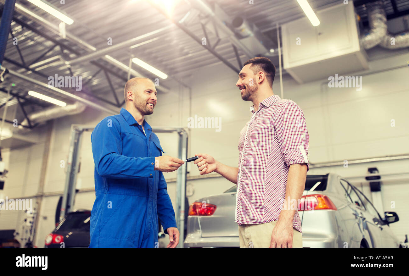 Mécanicien auto clé donnant à l'homme au magasin de voitures Banque D'Images