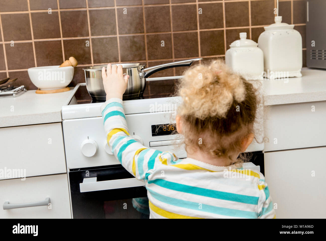 Accident en attente de se produire. Bébé fille tirant pot d'eau bouillante de l'eau dans la région de home cuisine. Risque de brûler la peau, accueil concept( mis en place, le pot est vide). Banque D'Images