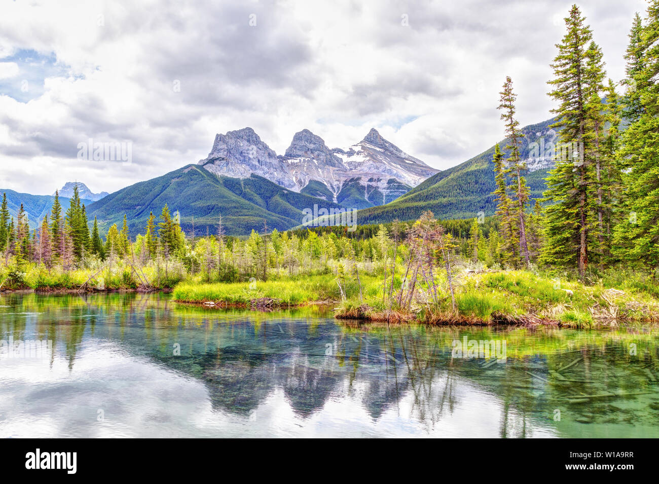 Canmore célèbre Trois Sœurs des pics de montagne et leurs réflexions sur la rivière Bow dans le sud de la gamme Banff Canadian Rockies sur un ciel nuageux S Banque D'Images