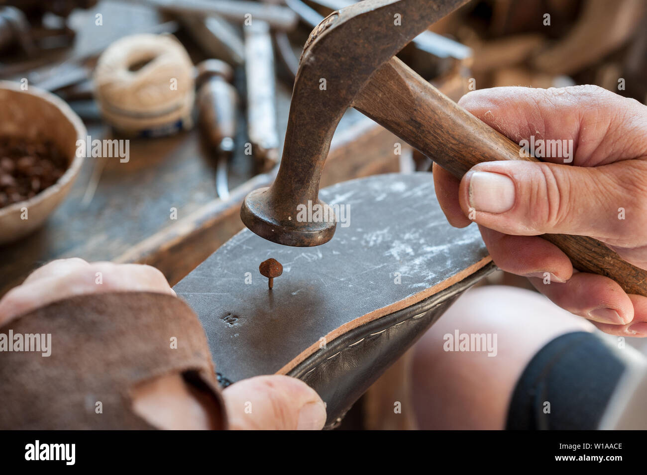 Shoemaker applique une balle sur la semelle d'une chaussure. Divers outils et instruments sont placés sur la table de travail. Banque D'Images