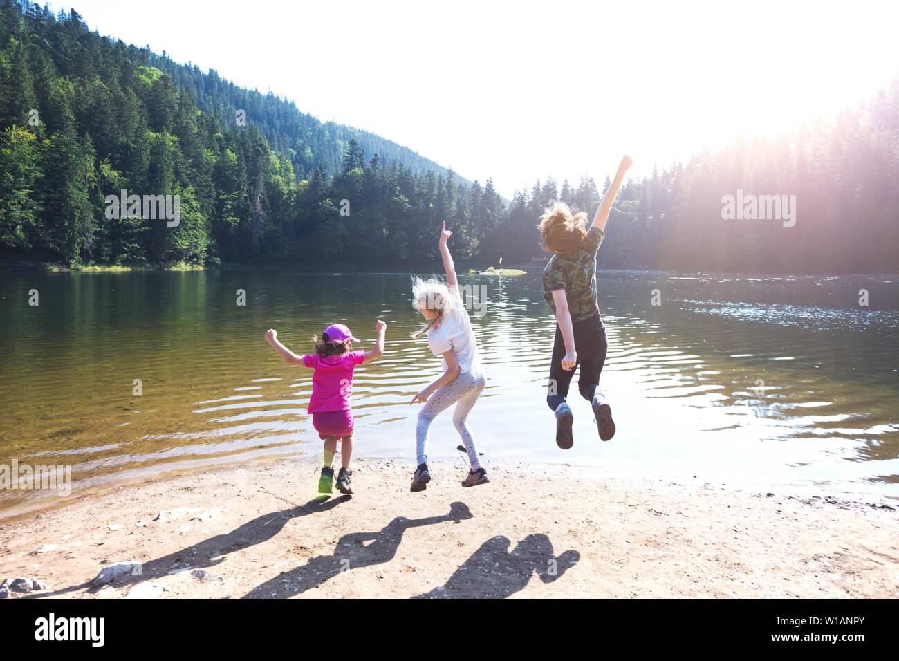 Été - trois soeurs sur une randonnée. Fun heureux famille sautant sur le rivage d'un lac de montagne synevyr. Banque D'Images