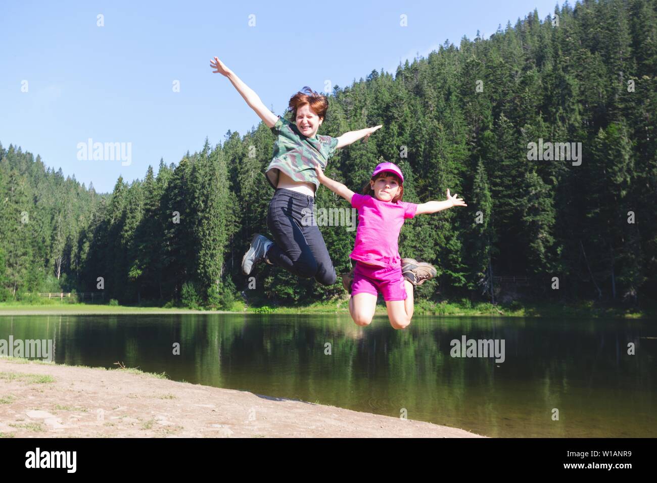 Été - deux soeurs en randonnée. Fun heureux famille sautant sur le rivage d'un lac de montagne synevyr. Banque D'Images