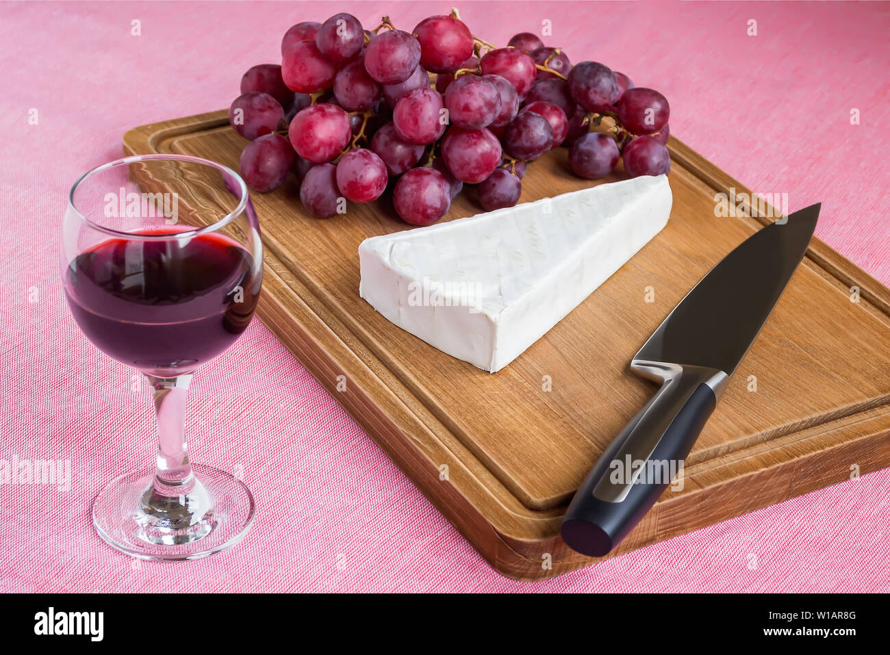 Verre de vin rouge et d'une pièce triangulaire de fromage Brie, raisins rouges doux, couteau chef sur une planche à découper en bois brun. Fromage à pâte molle moule comestible Banque D'Images
