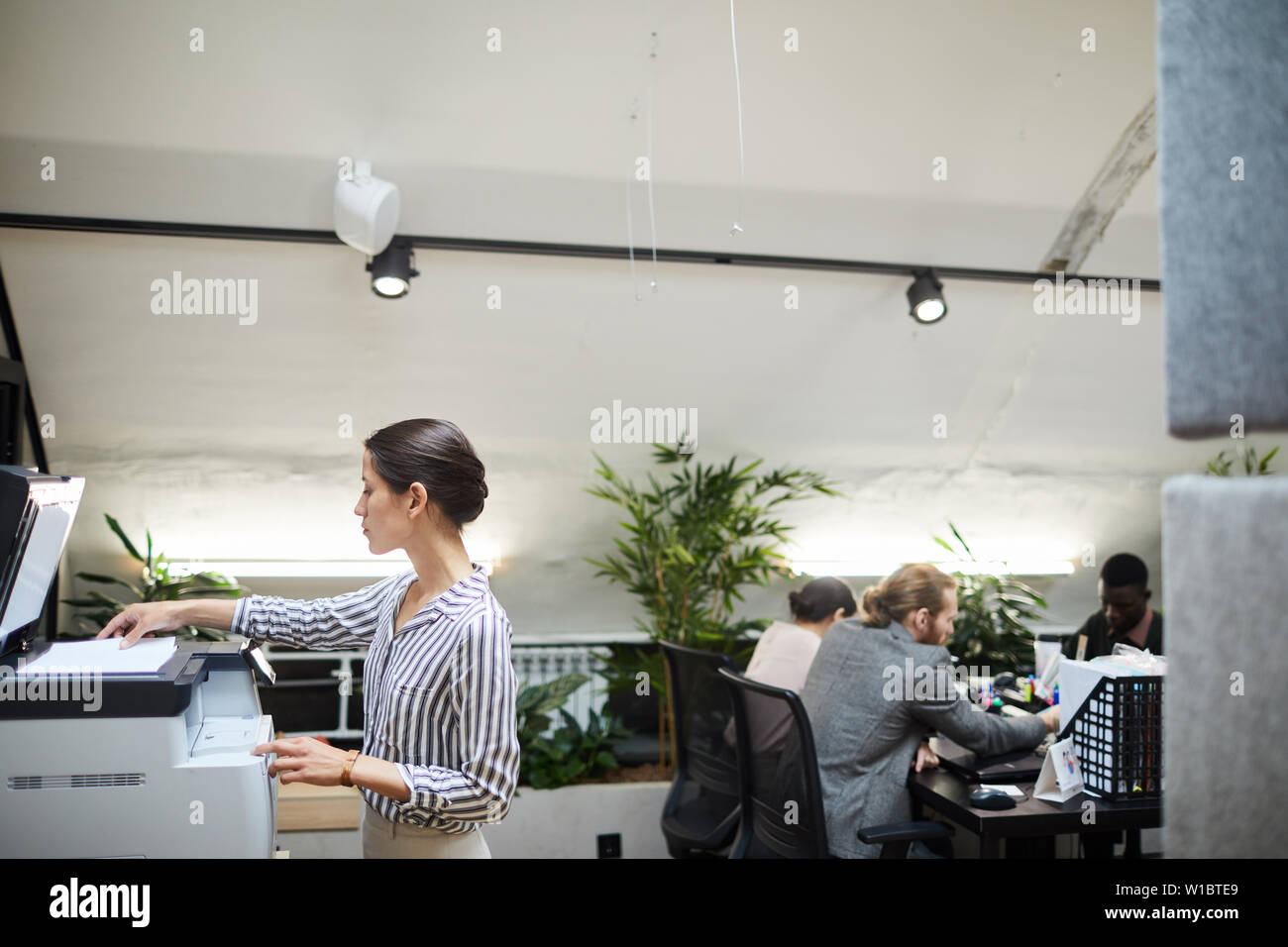 Side view portrait of young businesswoman la numérisation de documents tout en travaillant dans office, copy space Banque D'Images