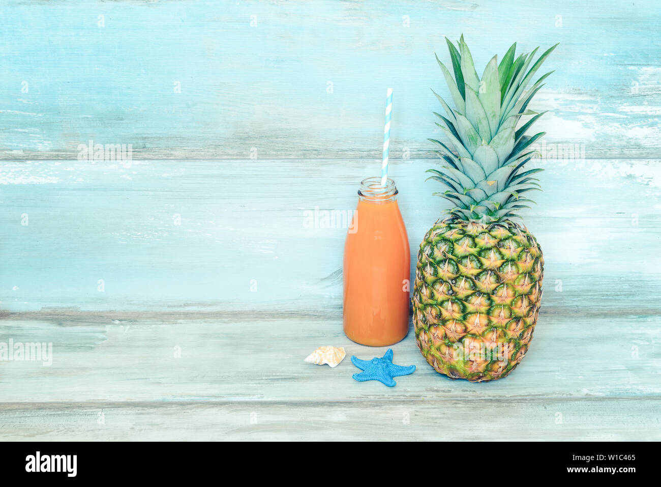 Concept d'été stillife - venu d'ananas et une bouteille de jus multivitaminé devant un fond bleu en bois rustique. Banque D'Images