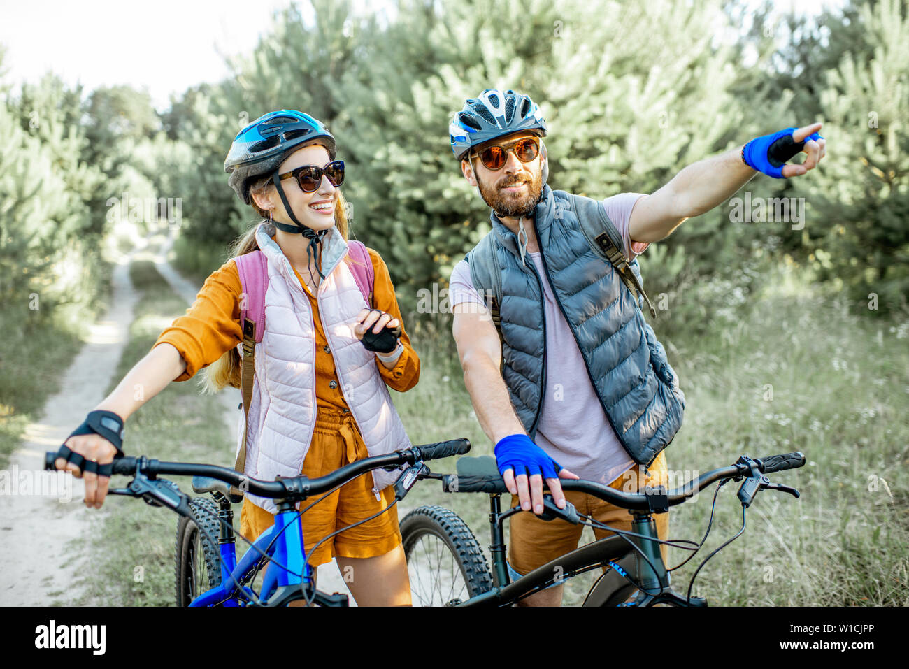 Jeune couple voyageant avec des vélos de montagne dans la forêt, montrant l'homme avec la main sur la voie à suivre Banque D'Images