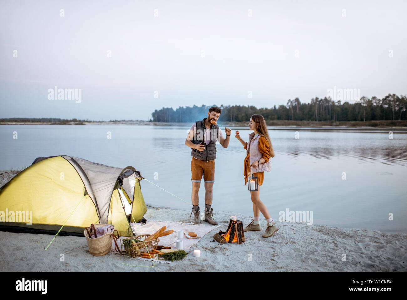 Young couple having fun at le camping sur la plage, debout près de la cheminée dans la soirée Banque D'Images