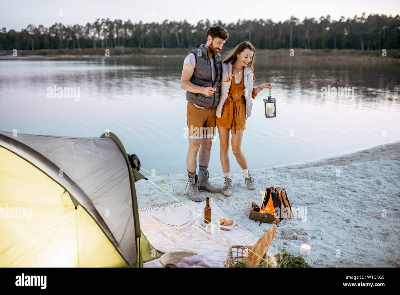 Young couple having fun at le camping sur la plage, debout près de la cheminée dans la soirée Banque D'Images