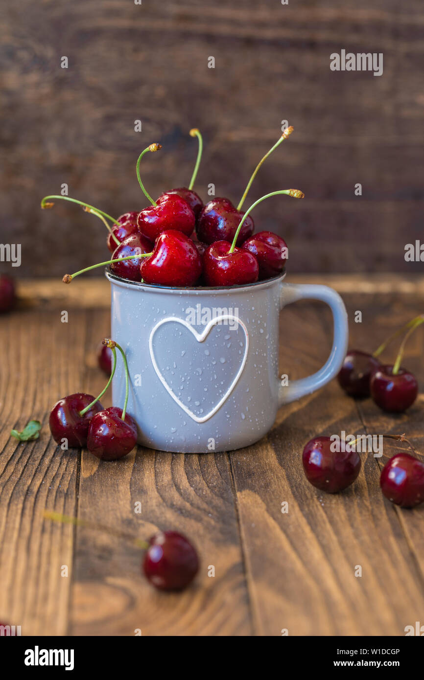 Cerises fraîches en gris tasse en forme de coeur sur table en bois, teinté Banque D'Images