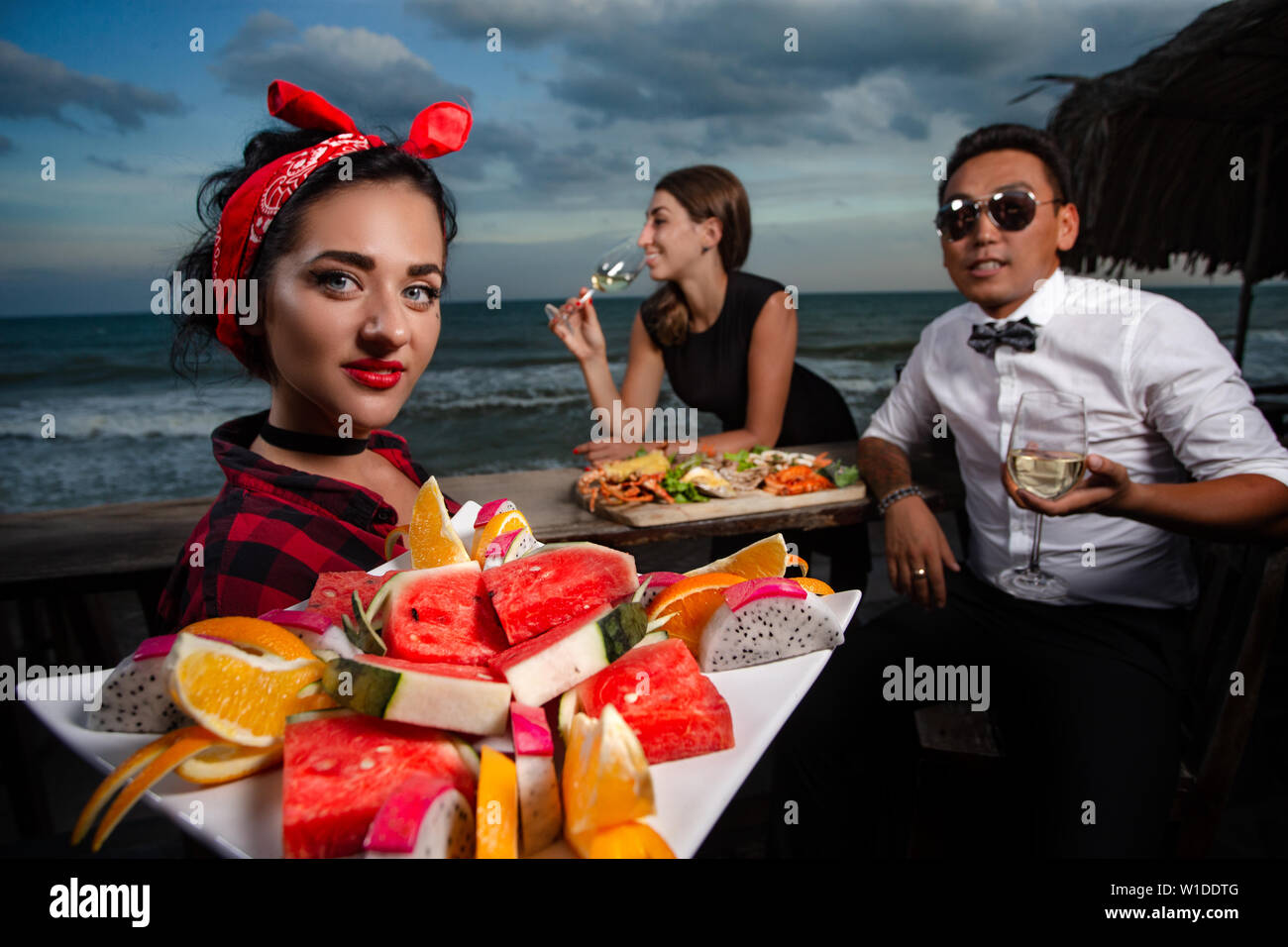 Amis dans un restaurant de fruits de mer - cheers clink verres et serveuse avec fruit dans l'avant-plan Banque D'Images