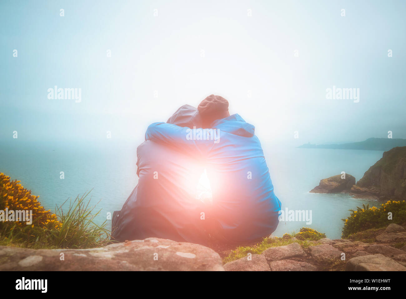 Ou arrière vue arrière de jeunes amoureux assis l'un contre l'autre et s'étreindre sur une falaise, regardant un paysage marin pittoresque avec des Rafale. L'amour, la romance, Banque D'Images