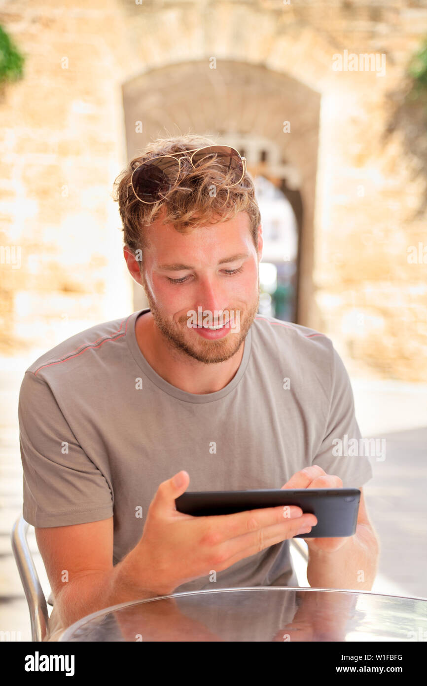 L'homme à l'aide de tablet 4g app travaillant dans le café en plein air. Les jeunes adultes mâles de race blanche écrit sur une tablette ou un guide de lecture e réservez en ligne pendant les vacances. Banque D'Images