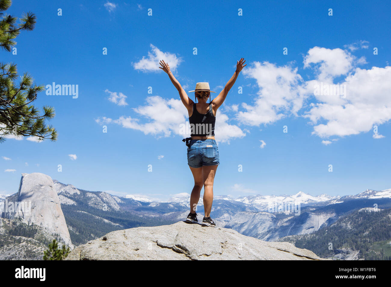 Femme de tourisme caucasienne dans sa trentaine avec des armes ouvertes de son dos face au parc national de Yosemite et demi-dôme de Glacier point, Californie, États-Unis Banque D'Images