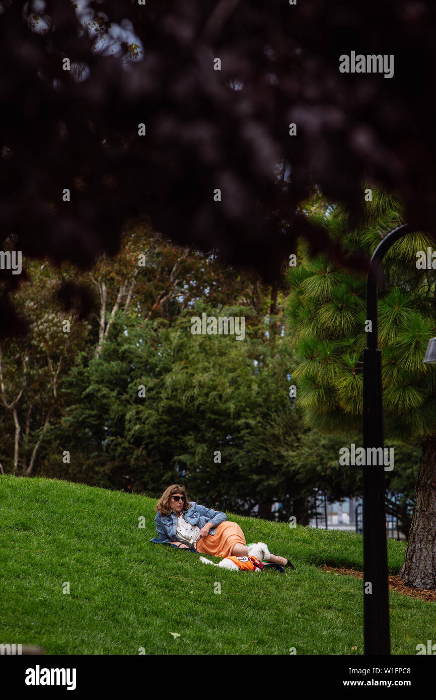 Une femme a posé sur l'herbe avec son chien dans un parc (Levi's Plaza) à San Francisco, Californie, États-Unis Banque D'Images