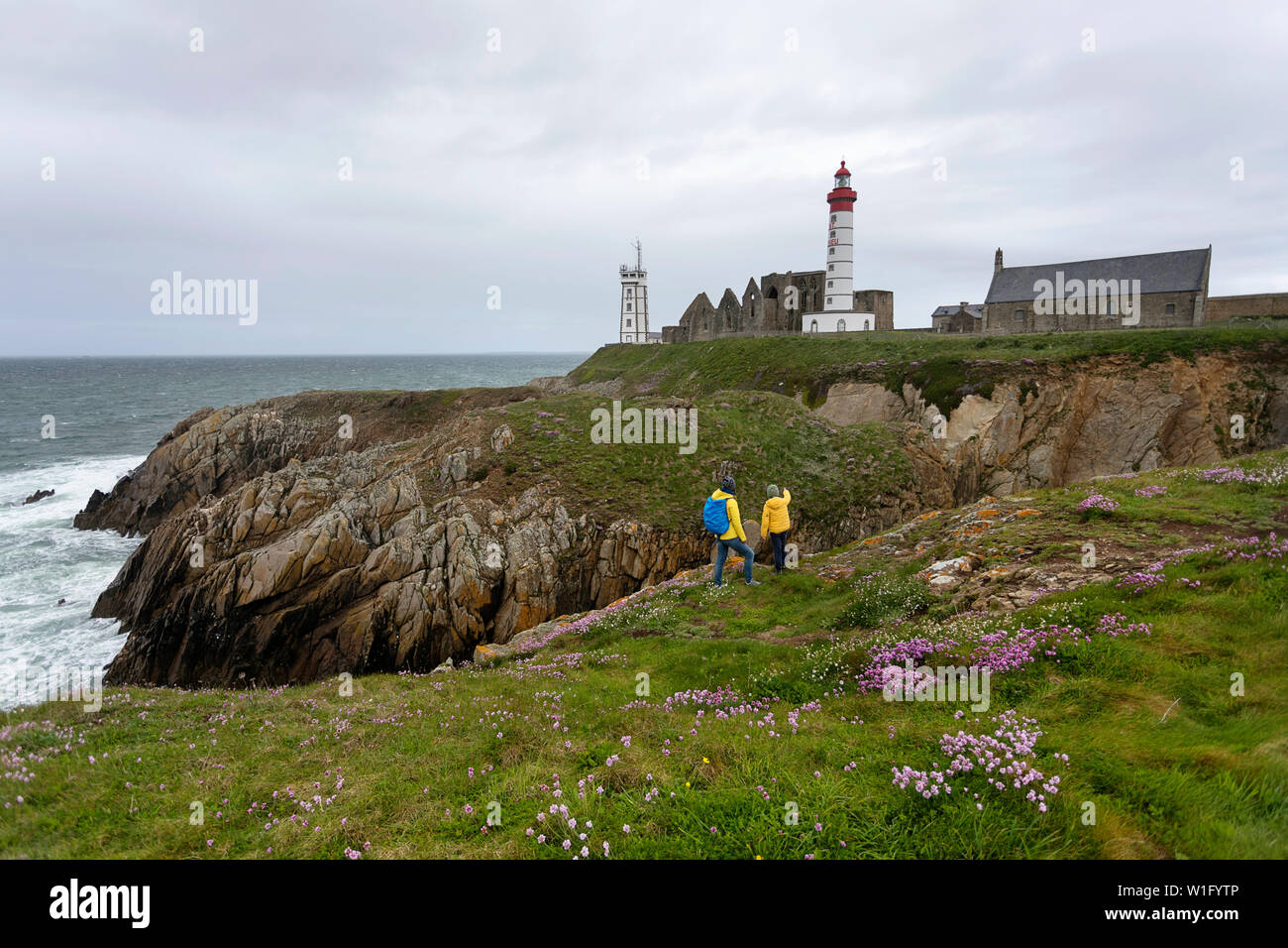 La mère et le fils debout sur clifs par le phare et l'abbaye s'élevant au-dessus de la mer et la côte rocheuse de la Pointe Saint-Mathieu en Bretagne, France Banque D'Images