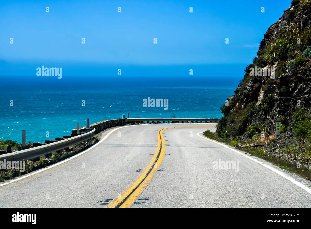 L'autoroute 1 en Californie panneaux autour d'une falaise avec l'océan bleu en arrière-plan. Banque D'Images