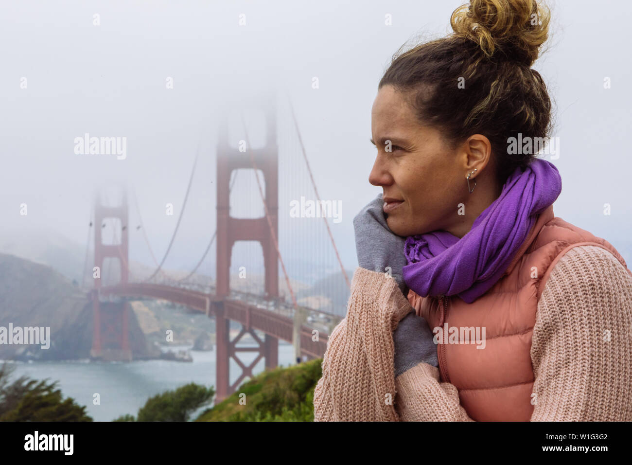 Cheveux bouclés Femme caucasienne dans sa trentaine avec un petit pain posant avec Golden Gate Bridge à San Francisco, Californie, Etats-Unis Banque D'Images