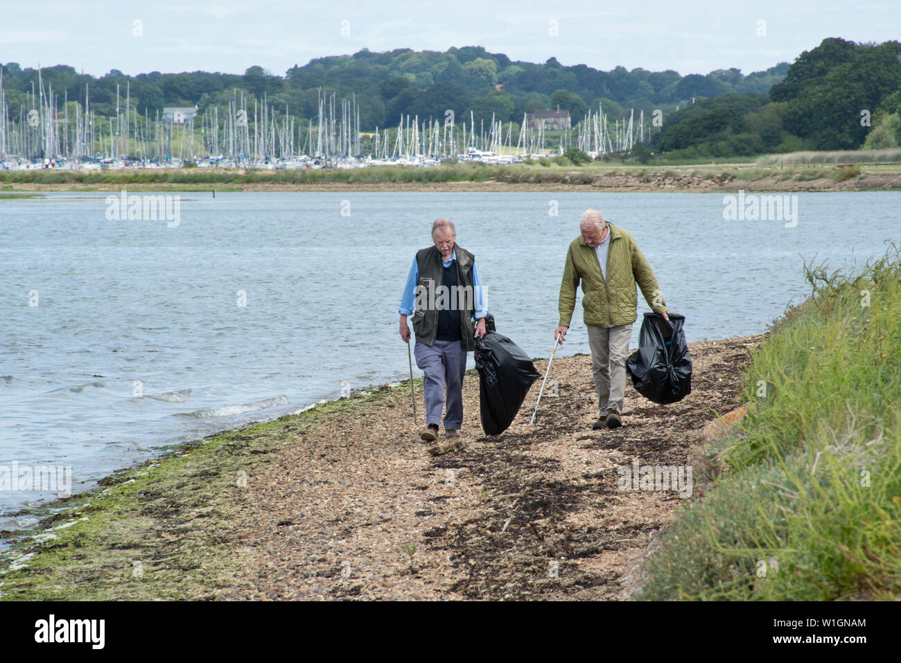 Deux hommes âgés d'effectuer un nettoyage de la plage. Les bénévoles avec des sacs poubelle noirs marchant le long d'une plage de galets. Banque D'Images