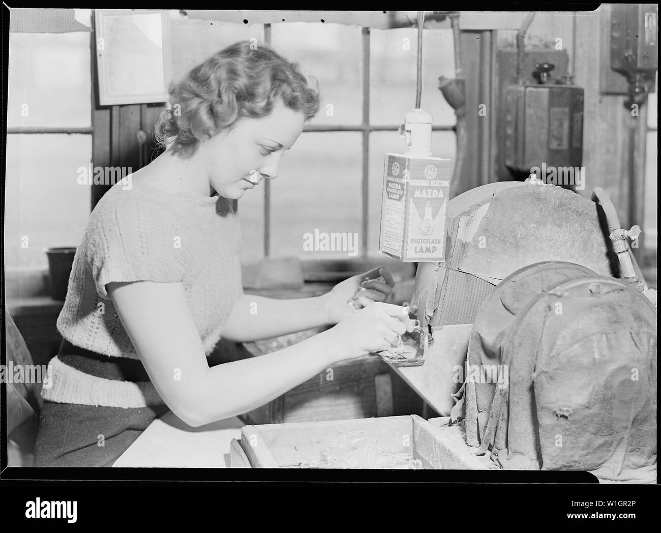 Millville, New Jersey - Bouteilles en verre. Un travailleur qualifié au T.C. Meulage Wheaton bouchons en verre pour bouteilles en verre. Une roue d'émeri a tourné à l'intérieur du boîtier à droite de la lampe. La jeune fille appuie sur la butée contre la roue d'émeri et lisse au large les bords. C'est à elle de juger de la taille du bouchon et de le façonner en conséquence. Banque D'Images