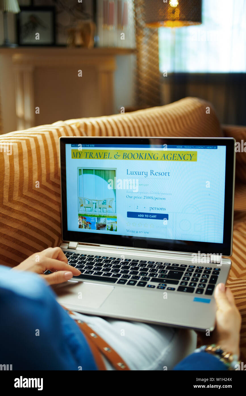 Jeune femme assise sur le canapé dans le salon moderne à sunny chaude journée d'été réservation en ligne chambre d'hôtel sur un ordinateur portable. Banque D'Images