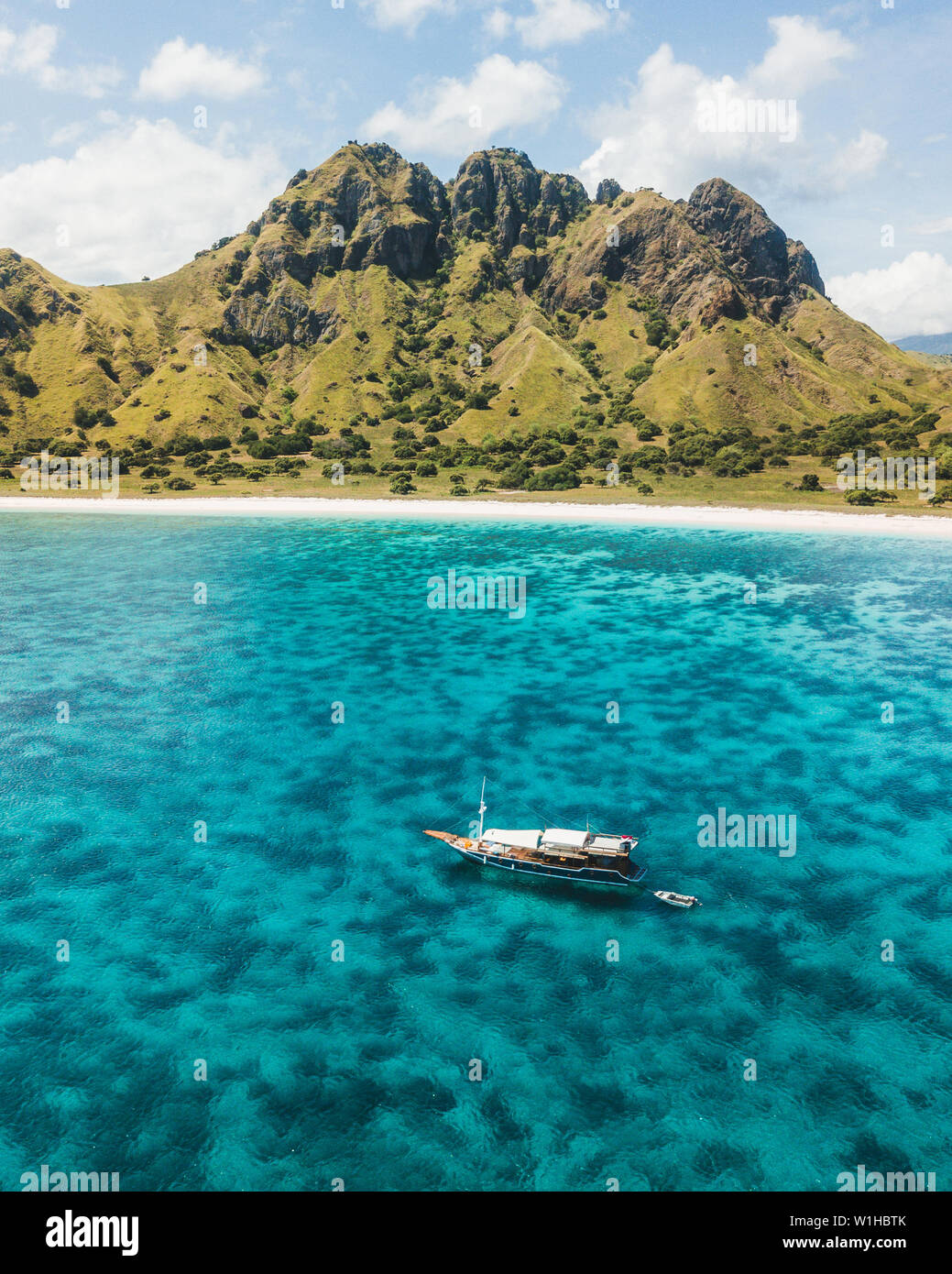 Bateau de croisière naviguant sur les récifs coralliens avec une plage tropicale et sur la montagne. Vue aérienne. L'île de Padar, Komodo en Indonésie. Banque D'Images