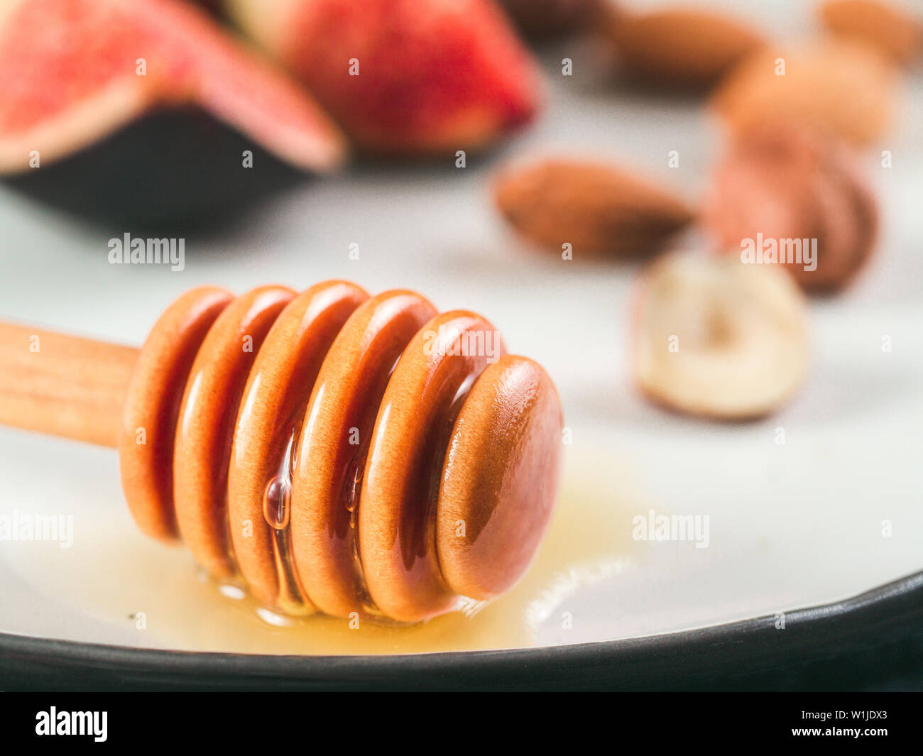 Vue rapprochée du miel le balancier et gouttes de miel sur la plaque. Shallow DOF. Les figues et les écrous à l'arrière-plan. L'espace de copie pour le texte. Banque D'Images