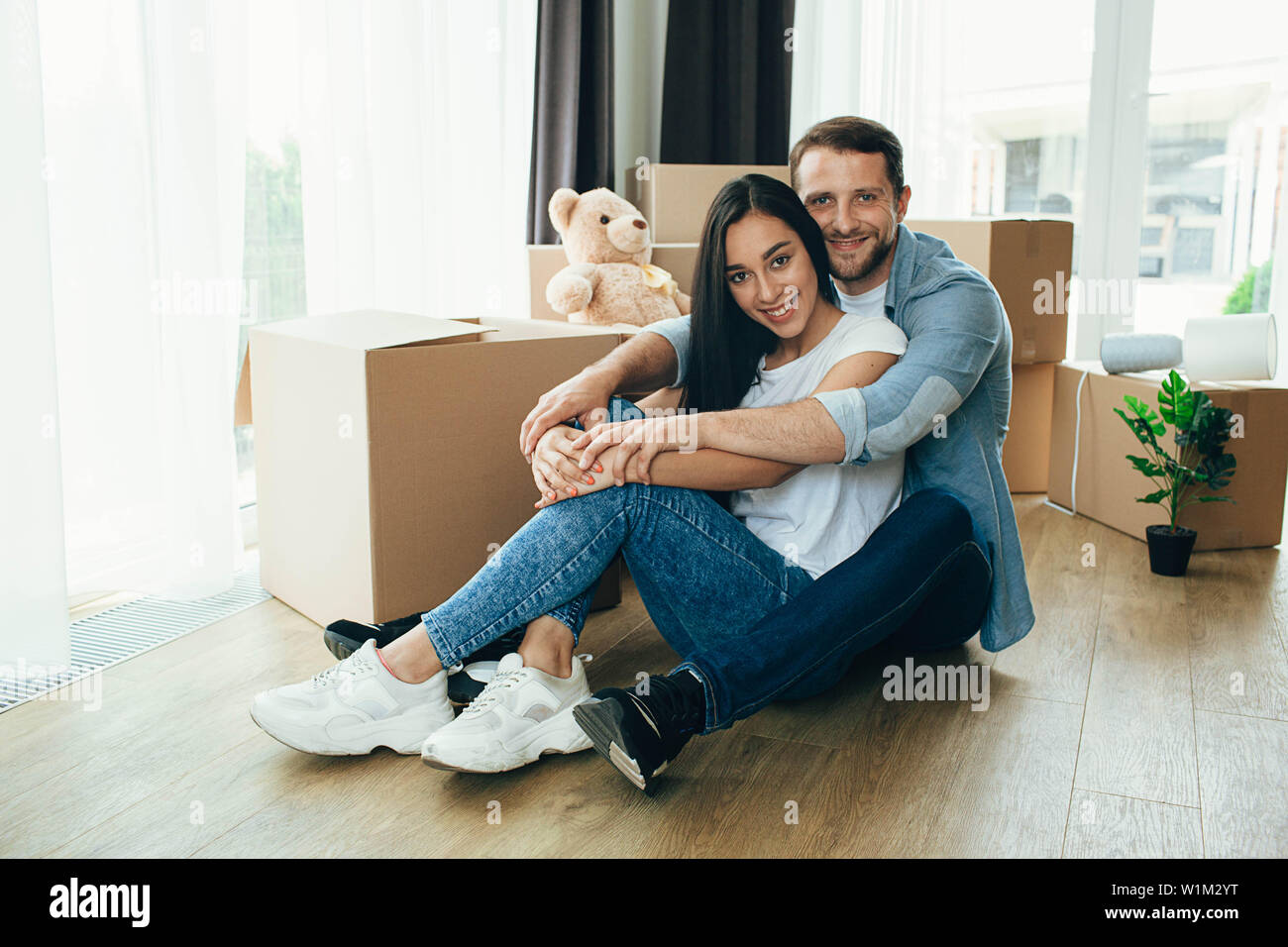 Man hug sa jeune épouse, la séance lors d'une nouvelle maison. Déménagement nouvel appartement, jeune couple location maison Banque D'Images