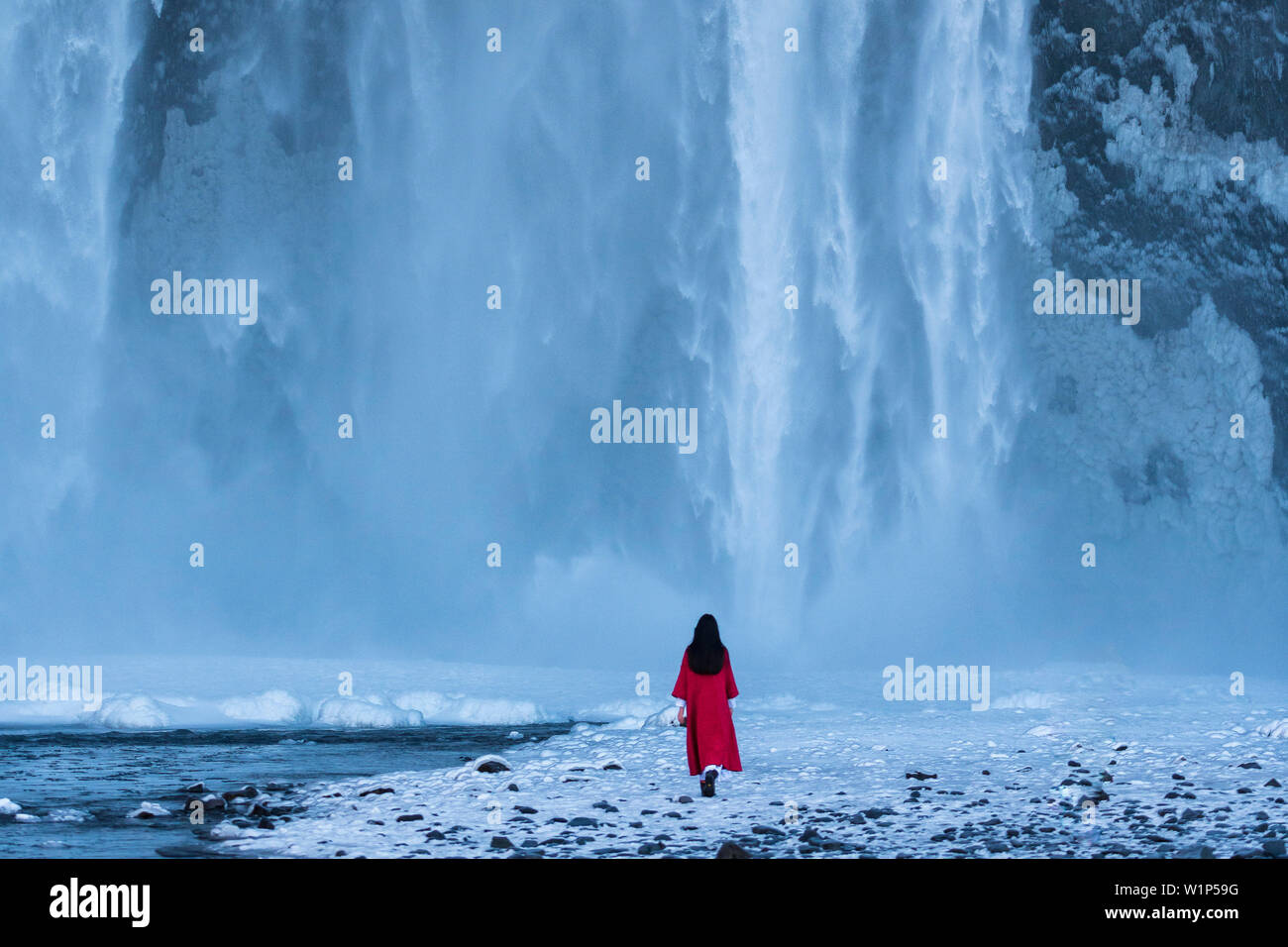 Les femmes dans un manteau d'hiver rouge en face de l'impressionnante cascade de Skogafoss, southcoast, Islande Banque D'Images