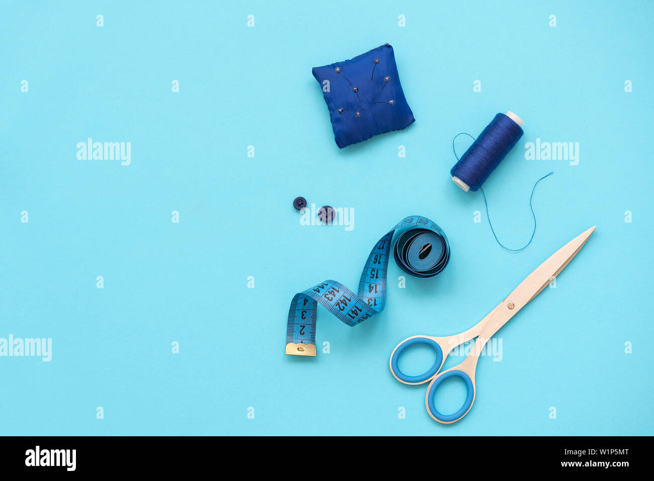 Accessoires de couture avec les threads, ciseaux, épingles, tissu, boutons et ruban de couture sur fond bleu. Vue d'en haut. Mise à plat. Banque D'Images