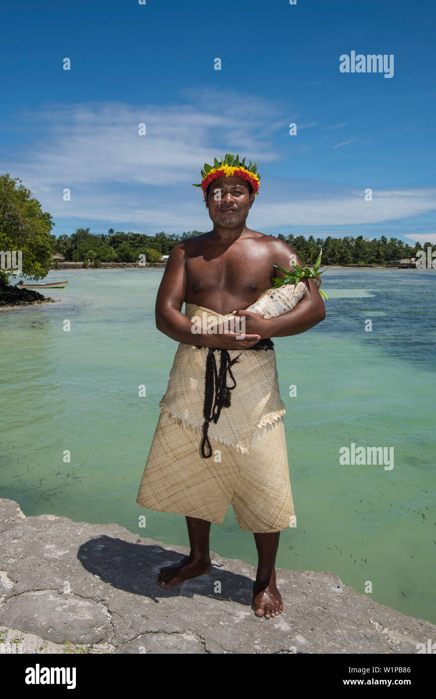 Un homme avec une feuille-et-couronne de fleurs et couvrant tout le corps fait de matière végétale, se dresse près de l'eau tenant un grand coquillage, l'Atoll de Butaritari, Gilbert Banque D'Images