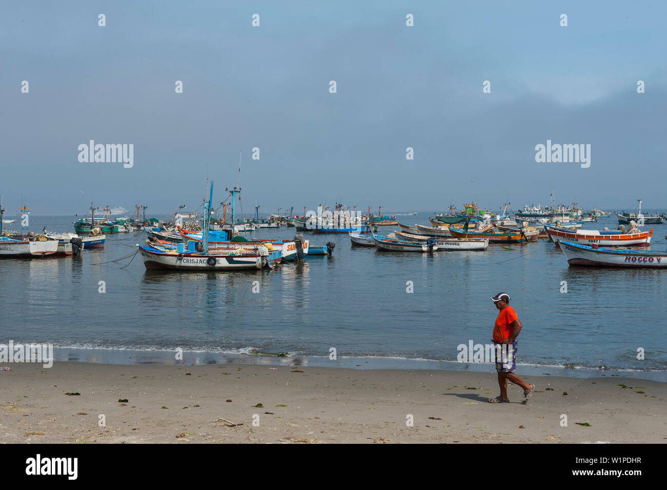 Un homme marche le long de la plage en face d'une toile de bateaux de pêche, Paracas, Ica, Pérou, Amérique du Sud Banque D'Images