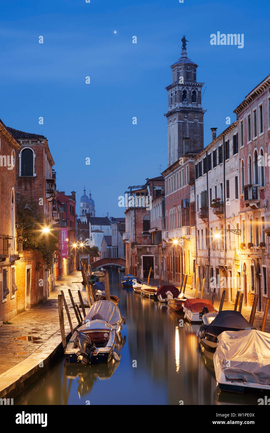 Maisons illuminées du Rio di San Barnaba avec la tour de l'église de Santa Maria dei Carmini et bateaux dans le bleu crépuscule, Dorsoduro, Venise, Ve Banque D'Images