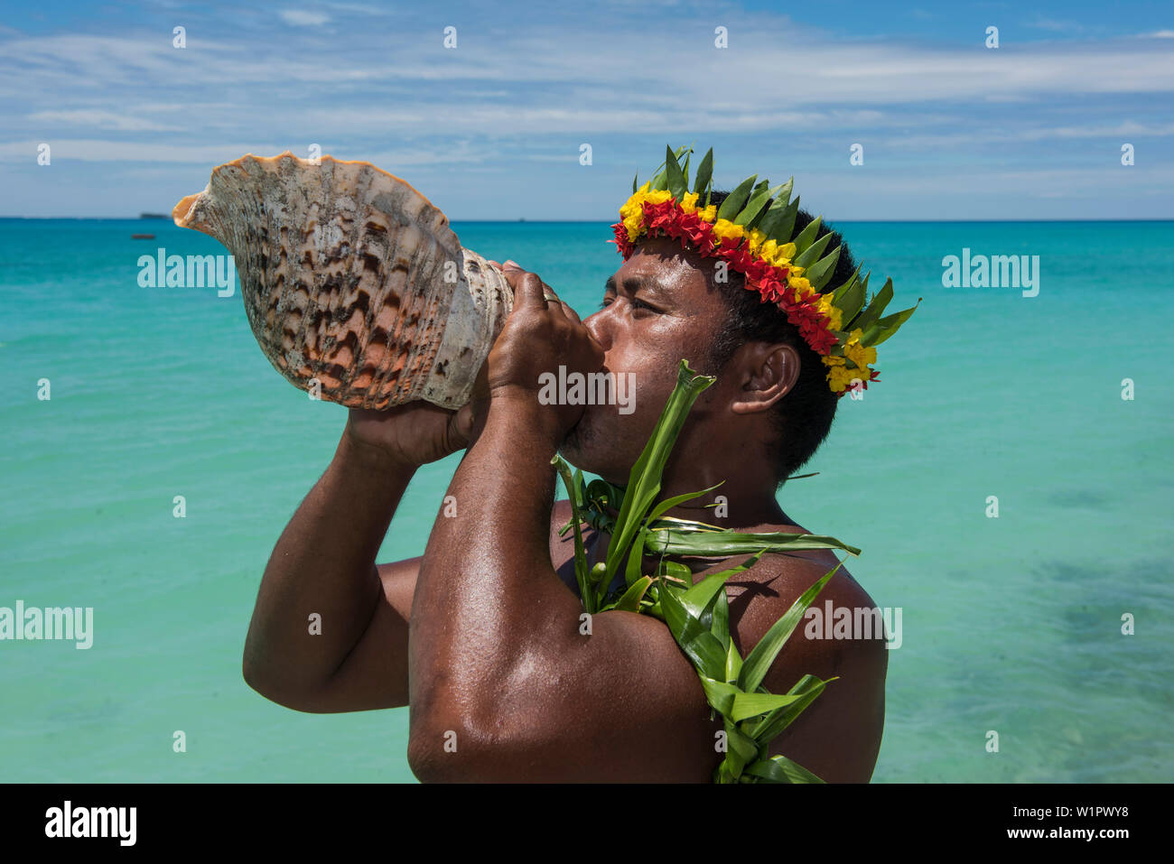 Un homme à la fleur et à feuilles souffle la couronne dans un grand coquillage d'annoncer l'arrivée de visiteurs d'une expédition en bateau de croisière, l'Atoll de Butaritari, Gil Banque D'Images