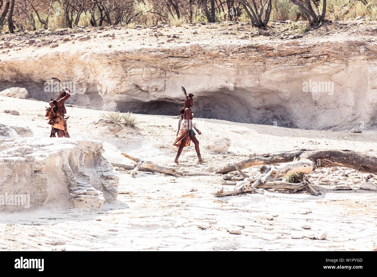 Deux femmes Himba, l'une d'entre elles portant son enfant, à la recherche de leur bétail dans une rivière à sec, Kunene, Namibie Banque D'Images
