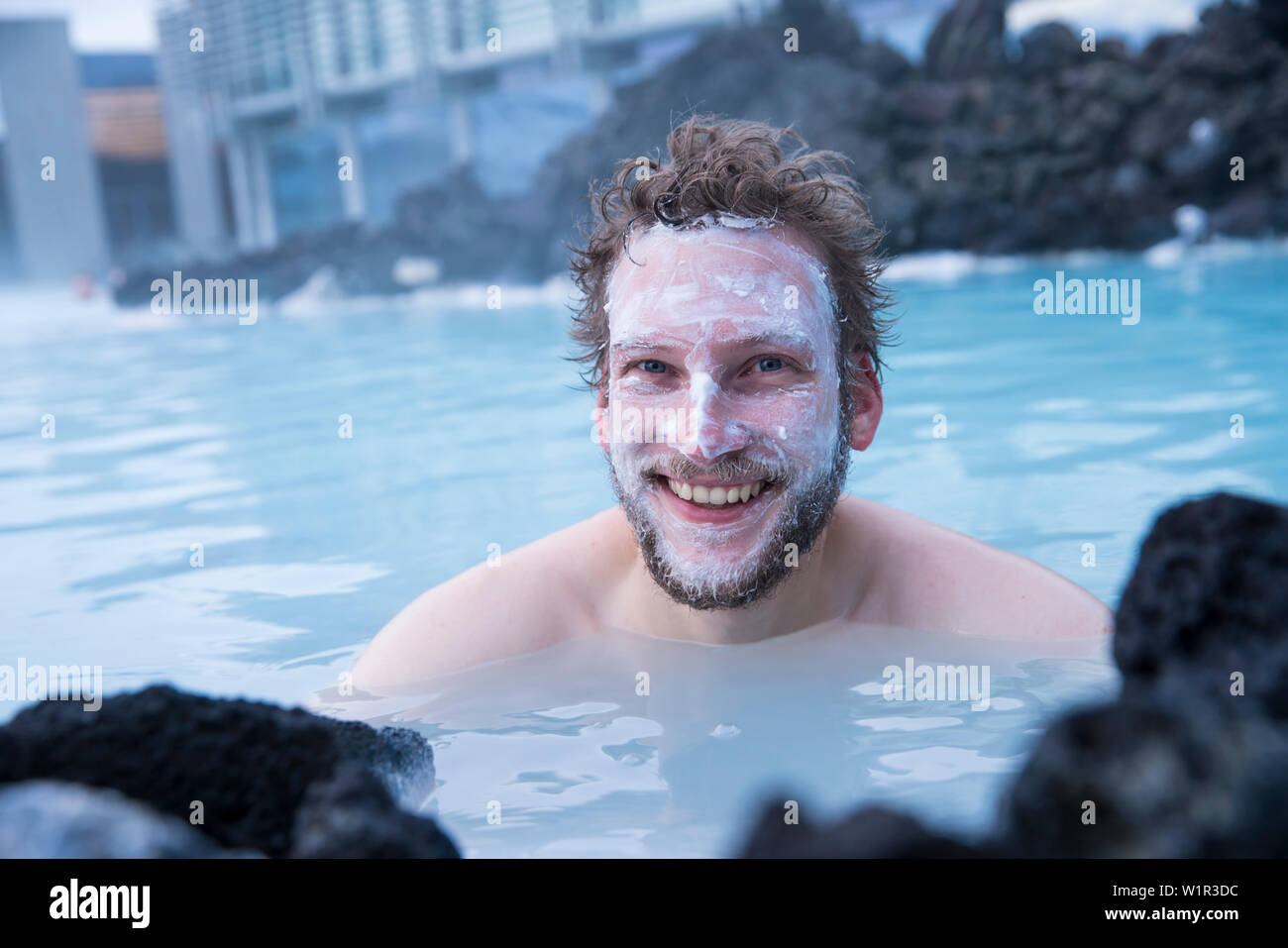 Jeune homme porte un masque de boue de silice et sourires pendant le bain au Blue Lagoon, le fameux wellness piscine thermale avec ses typiques de l'eau bleu-blanc dans Win Banque D'Images