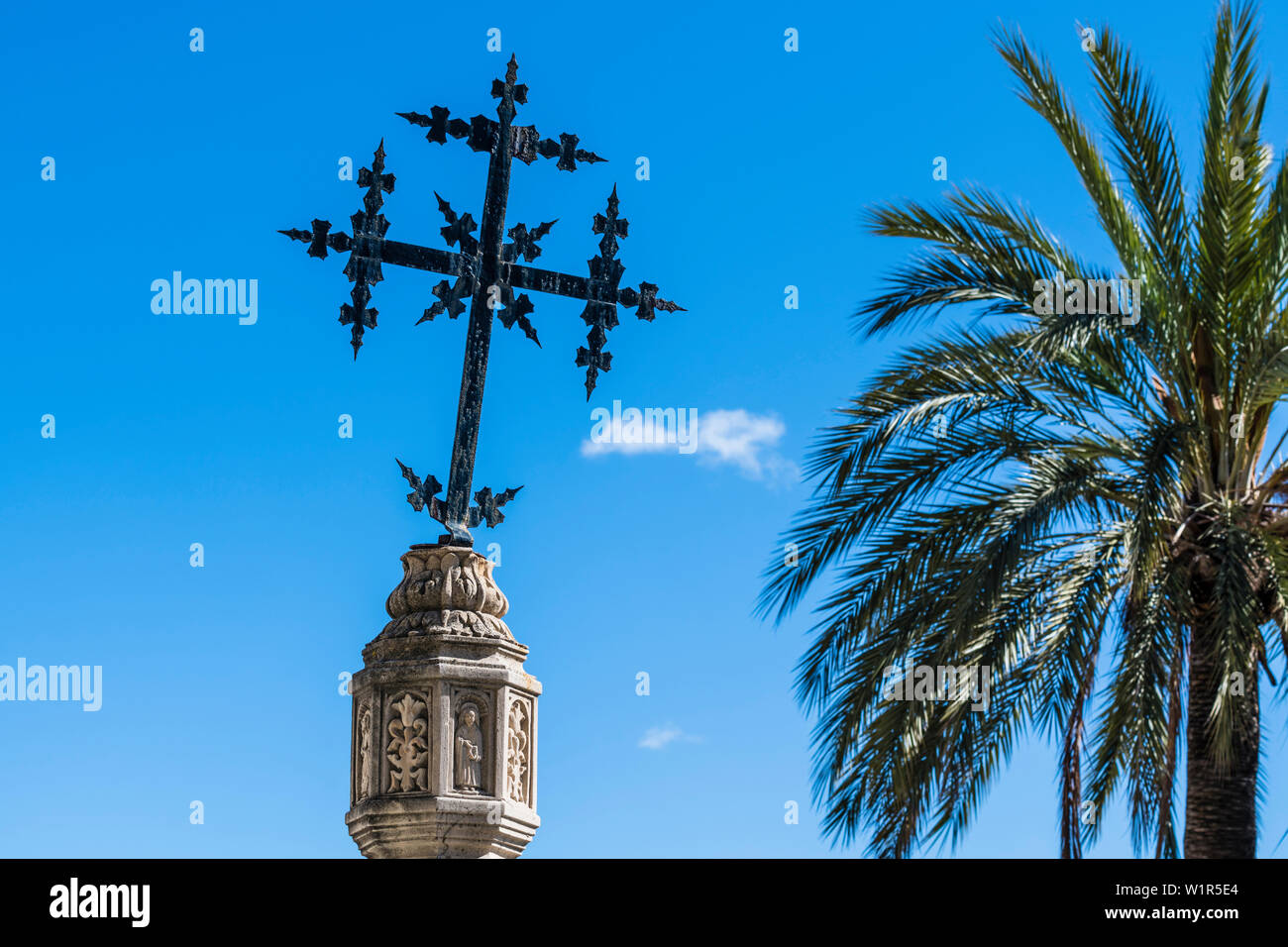 Une croix sur une colonne en pierre à côté d'un palmier en face de l'église, Selva, Majorque, Espagne Banque D'Images