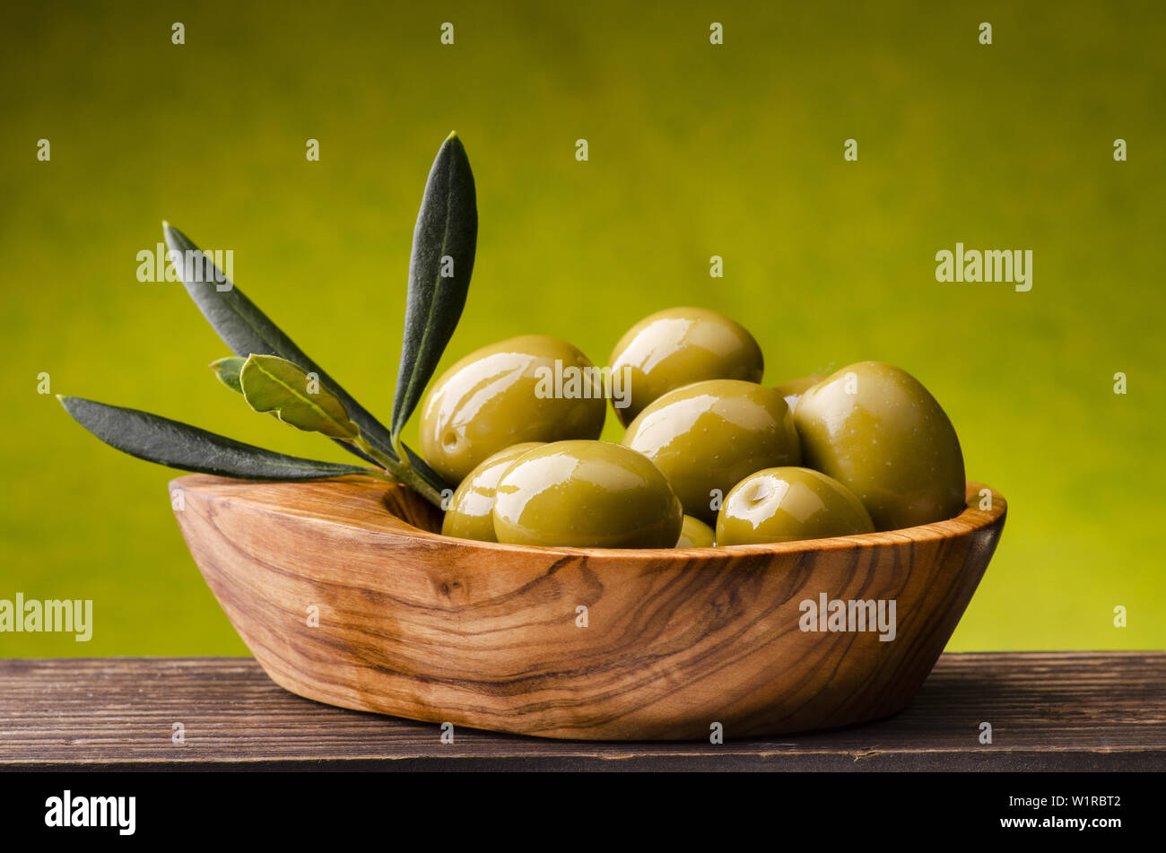 Bol en bois d'olivier plein d'olives vertes sur fond vert. Banque D'Images