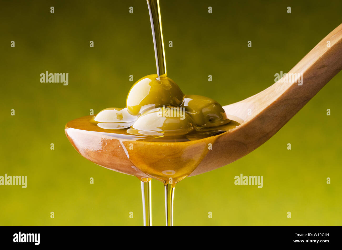 L'huile d'olive extra vierge flux sur un bol en bois plein d'olives vertes Banque D'Images