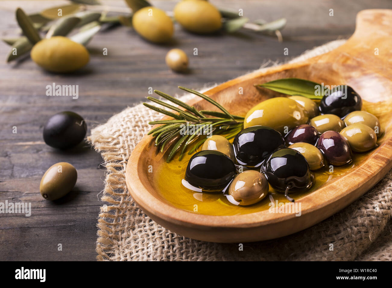 Bol en bois au premier plan avec le romarin olives et huile vierge sur la table en bois Banque D'Images